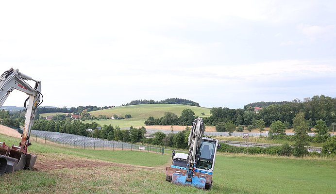 Montagesysteme für Solarpanele stehen links und rechts der Autobahn A96, davor stehen zwei Bagger.