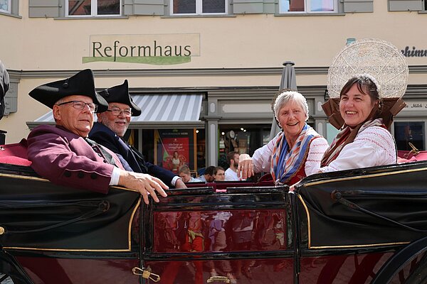 Kutsche mit zwei Männern und zwei Frauen in Tracht