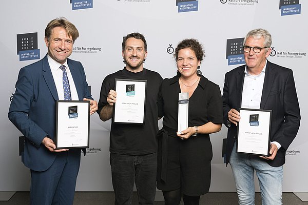 Drei Männer und eine Frau. Sie halten Urkunden und eine Art von Turm in der Hand