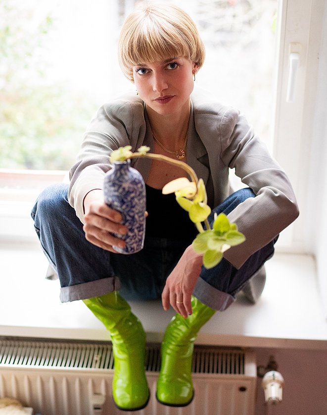 Eine Frau reicht dem Betrachter eine Blume.