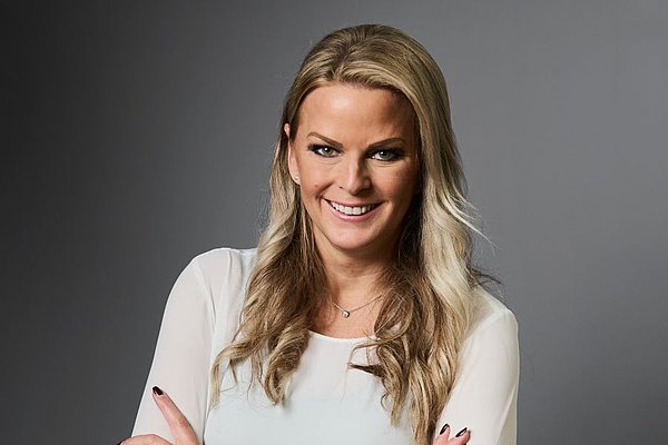 Eine Frau mit blonden langen Haaren lächelt freundlich in die Kamera.