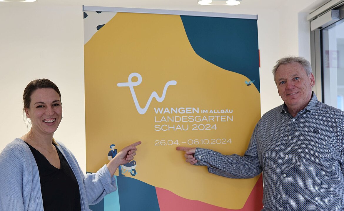 Eine Frau und ein Mann vor dem Logo der Landesgartenschau 2024.