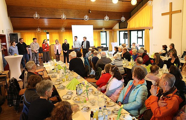 Viele Menschen an Tischen; eine Gruppe stellt sich vor