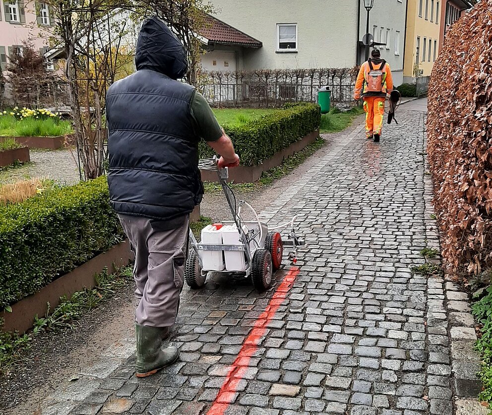 Zwei Bauhofmitarbeiter bringen den Roten Faden auf dem Weg auf.