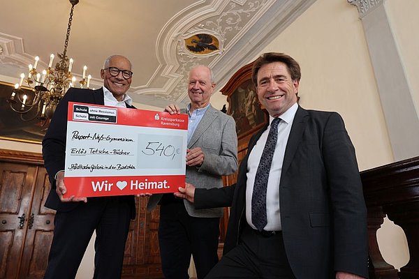 Drei Männer stehen auf einer Treppe und halten einen Scheck mit dem Betrag 540 Euro in die Kamera.