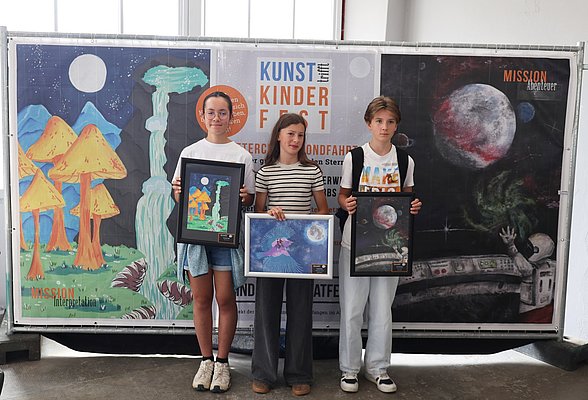 Drei Kinder stehen vor einem Plakat mit dem Titel "Kunst Kinderfest". Sie halten jeweils gerahmte Kunstwerke in den Händen. Im Hintergrund sind farbenfrohe, fantasievolle Landschaften, Planeten und Raumfahrt-Motive zu sehen.