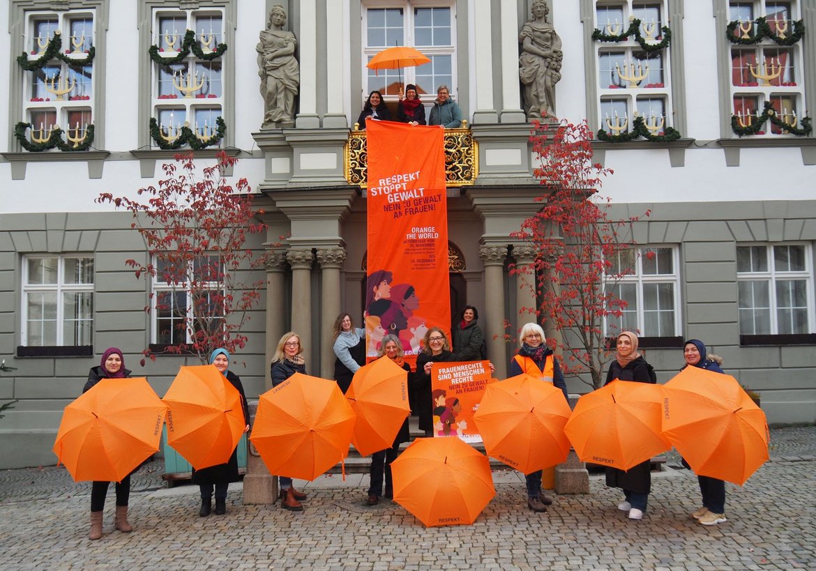 Frauen am Rathaus mit orangefarbenen Schirmen