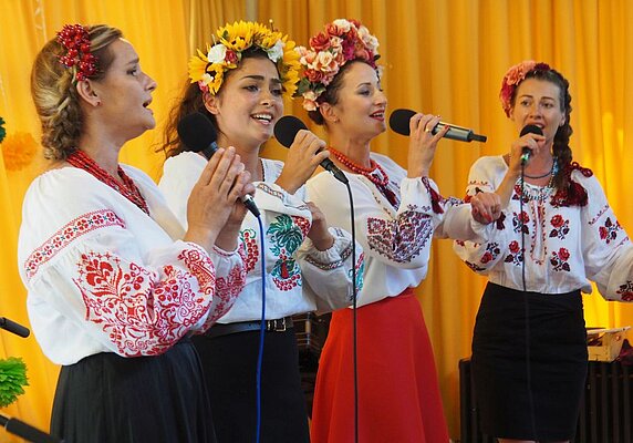 Frauen in bunten Blusen und mit Blumenkränzen im Haar singen