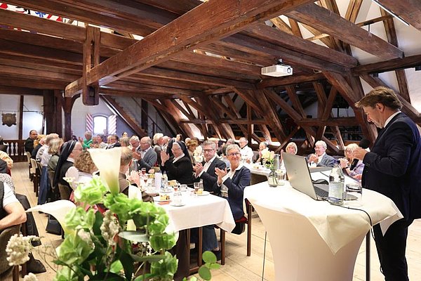 Blick in den festlich geschmückten Sitzungssaal, OB Lang spricht vor vielen Menschen, die an Tischen sitzen.