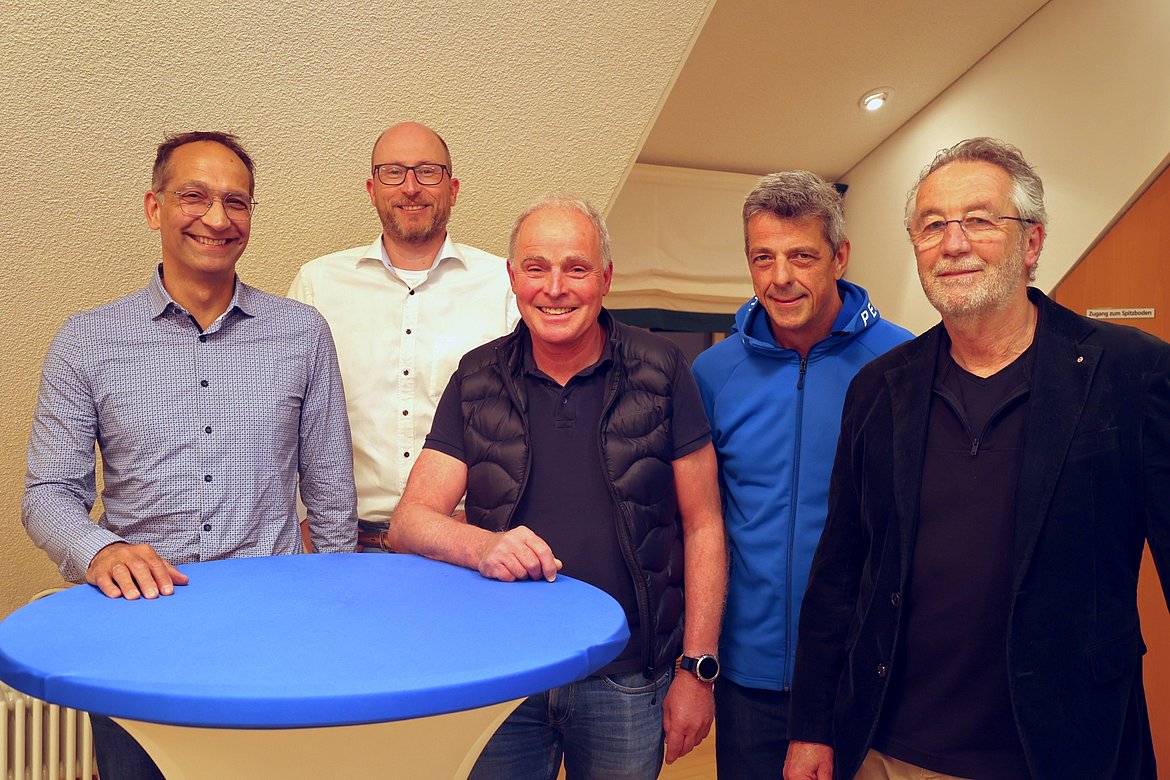 Fünf Männer an einem Stehtisch.