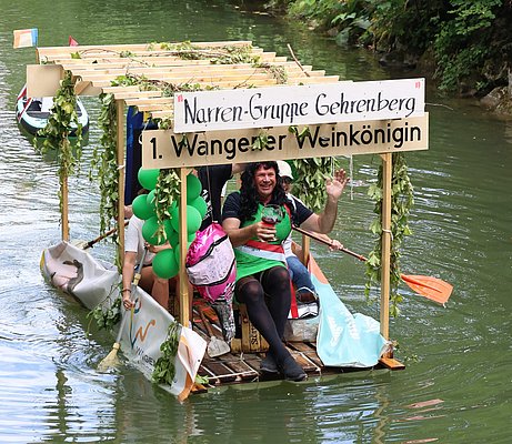 Auf einem Boot sitzt ein Mann verkleidet als Weinkönigin.