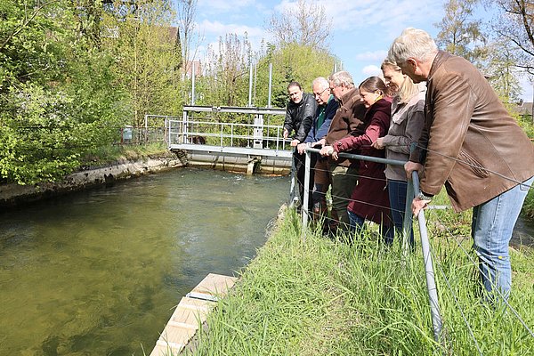 Mehrere Menschen schauen am Kanal auf eine Konstruktion aus Holz.