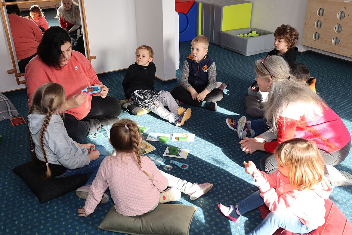 Kinder schauen auf Erzieherin. Sie zeigt ein Bild.