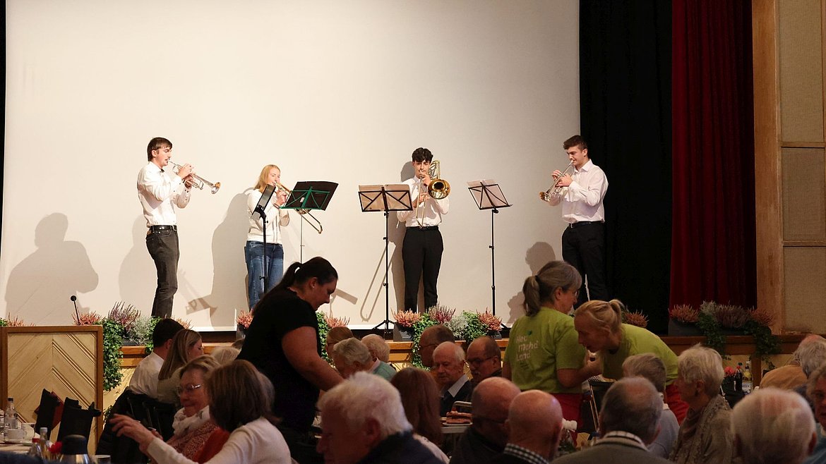 Vier Musiker auf der Bühne. Im Saal Menschen.