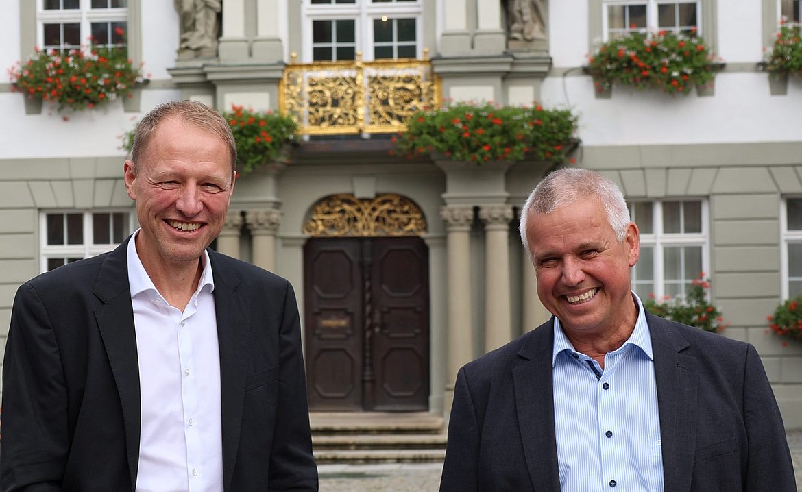 Zwei Männer vor dem Rathaus. Sie lachen.