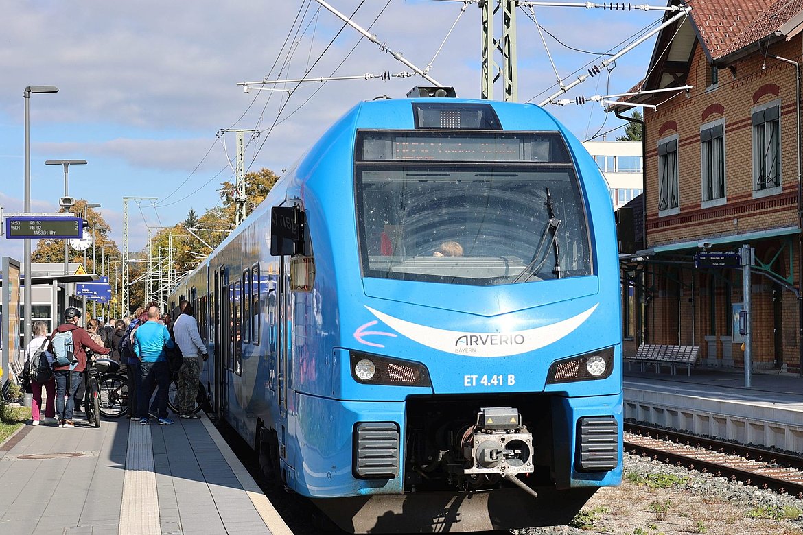 Blauer Zug auf am Bahnhof. Menschen steigen ein und aus.