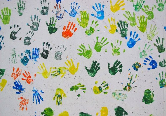 Viele bunte Handabdrücke auf einer weißen Wand.
