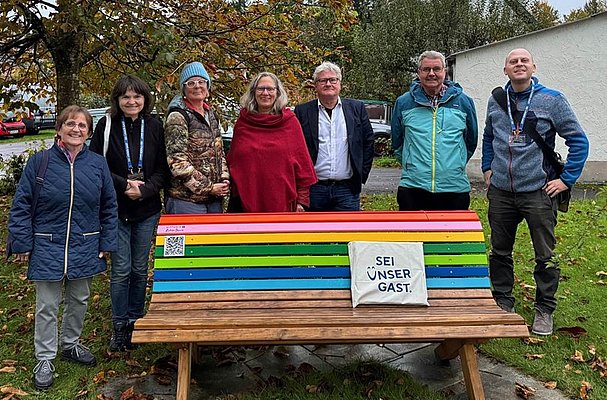 Gruppenbild mit sieben Personen an einer bunten Sitzbank