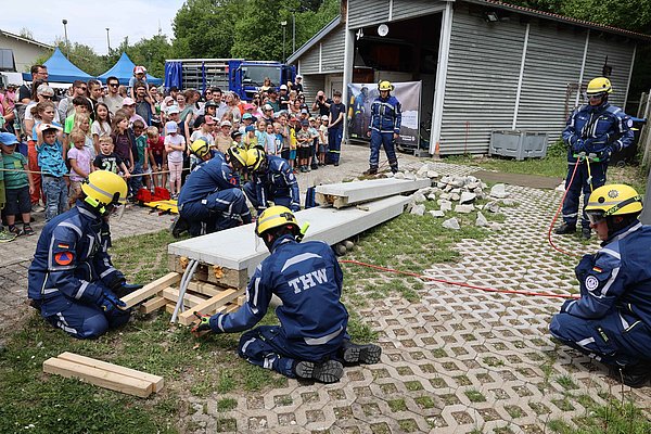 Zuschauer und THW-Team. Es pumpt ein Kissen unter einer Betonrampe auf, um eine Puppe zu retten.