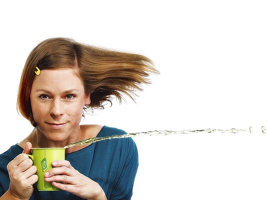 Eine Frau mit einer Tasse. Daraus spritzt Wasser.