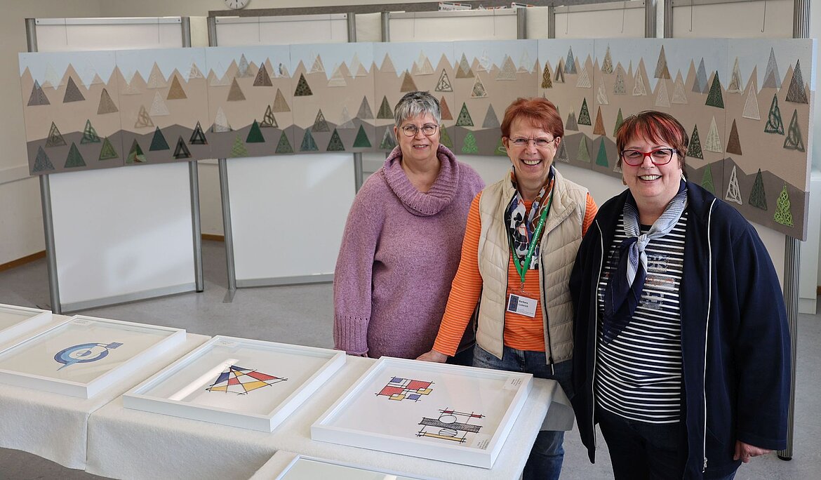 3 Frauen und ein Kunstwerk aus Spitze, das die Alpen darstellt.