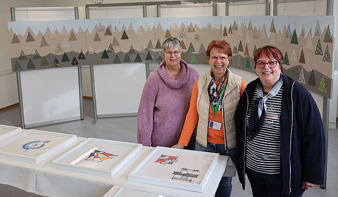 3 Frauen und ein Kunstwerk aus Spitze, das die Alpen darstellt.