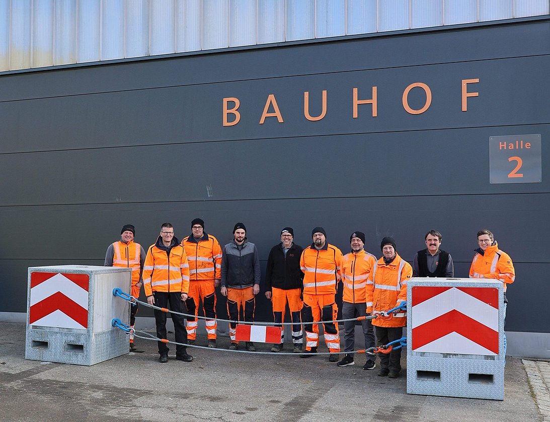 eine Gruppe von Männern des städtischen Bauhofs vor einer Wand und hinter eine Zufahrtssperre