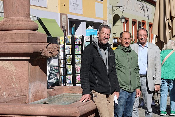 Drei Männer stehen neben einem Brunnentrog.