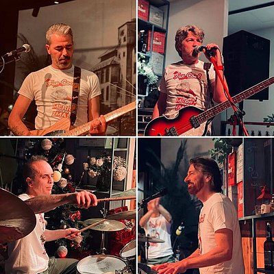 Vier Musiker in einem Raum, jede in einem separaten Quadrat. Oben links spielt ein Mann E-Gitarre, darüber ein anderer am Mikrofon. Unten links sitzt ein Drummer, rechts ein Mann mit Mikrofon. Alle tragen T-Shirts und sind in einer festlich dekorierten Umgebung.