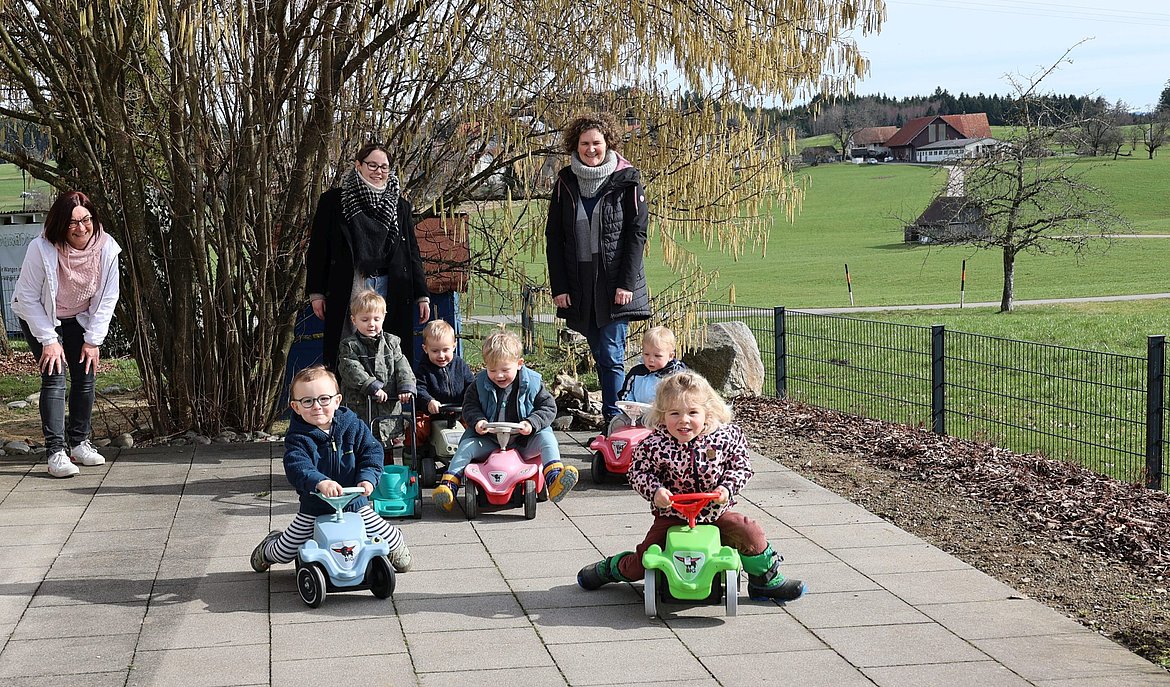 Kinder fahren auf dem Bobbycar um die Wette, drei Erzieherinnen schauen zu