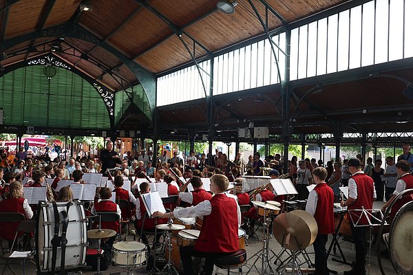 Eine Musikkapelle vor vielen Menschen in einer Markthalle 