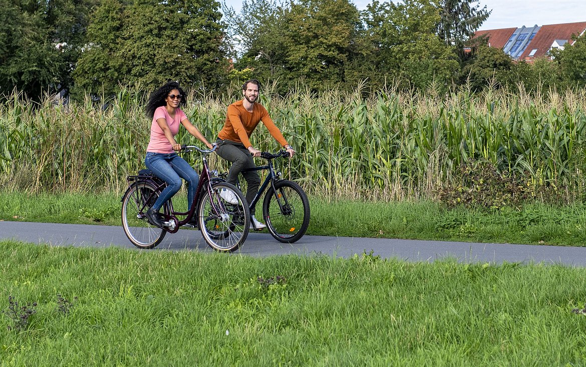 Ein Mann und eine Frau auf Fahrrädern vor einem Maisfeld.
